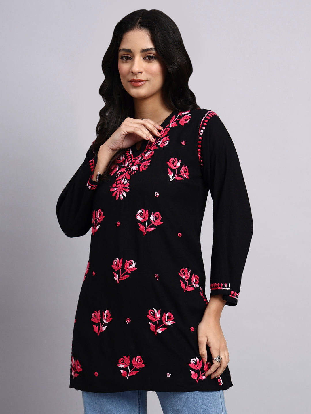Woman wearing a black floral embroidered top against a gray background