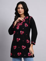 Woman wearing a black floral embroidered top against a gray background