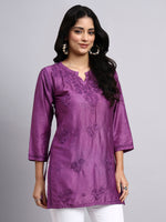 Woman wearing a purple embroidered kurta against a gray background