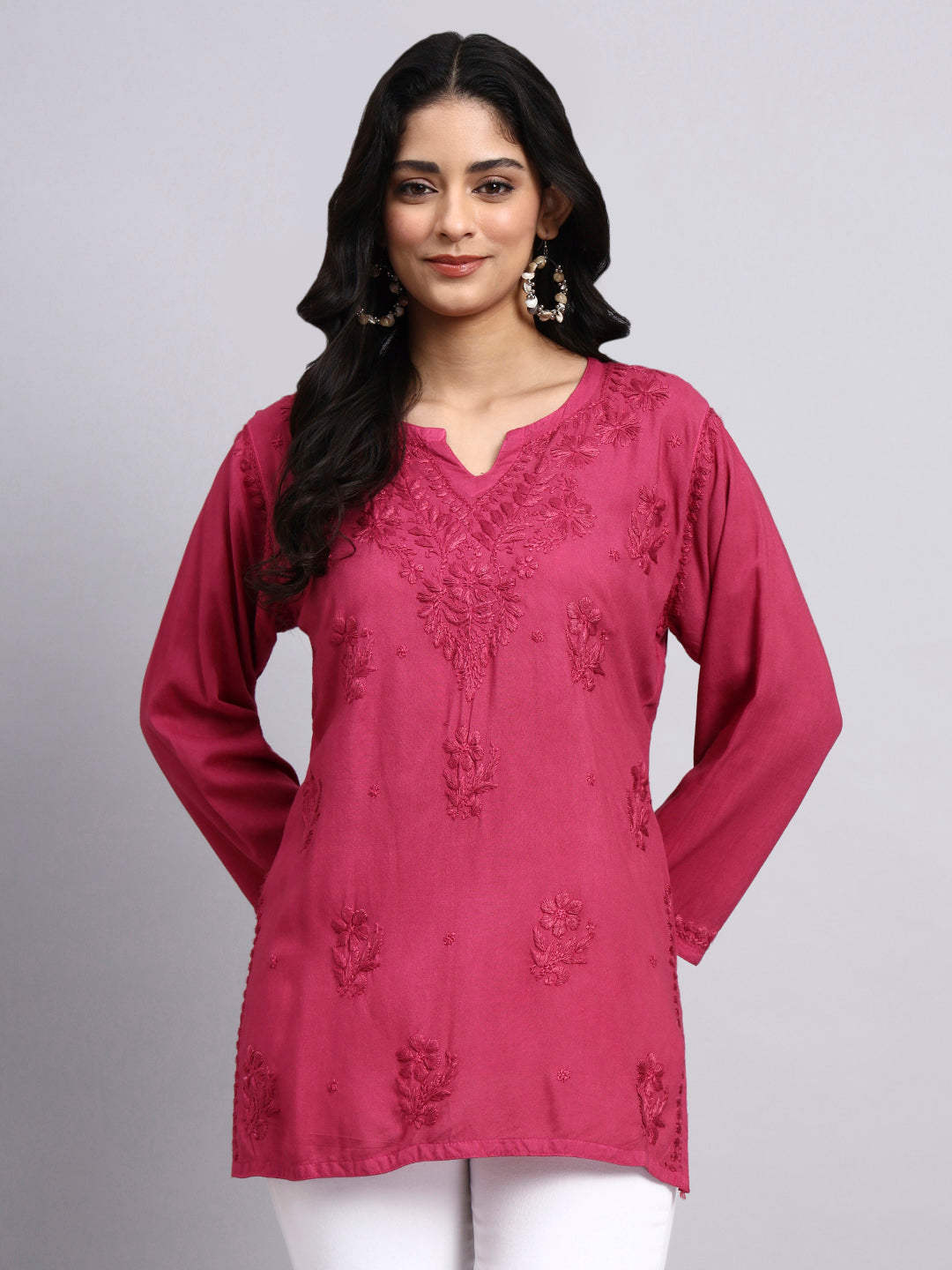 Front look of Woman wearing a pink embroidered top against a gray background