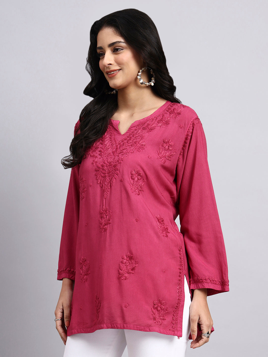 Side view of Woman wearing a pink embroidered top against a gray background