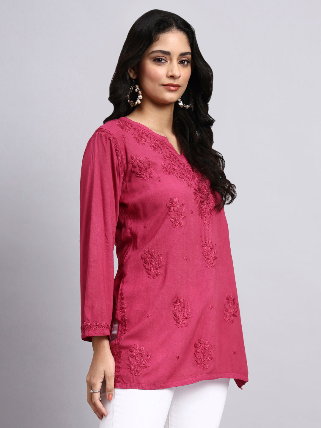 Woman wearing a pink embroidered top on a gray background