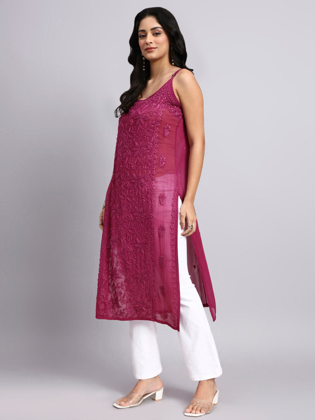 Side dress of Woman wearing a long rani pink embroidered dress with white pants on a gray background