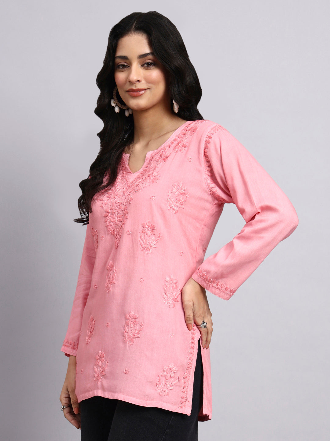 Side view of Woman wearing a pink embroidered top against a gray background