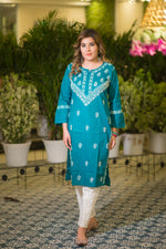 Front view of a woman in a teal blue long kurta that has white floral embroidery on the neckline and sleeves. 