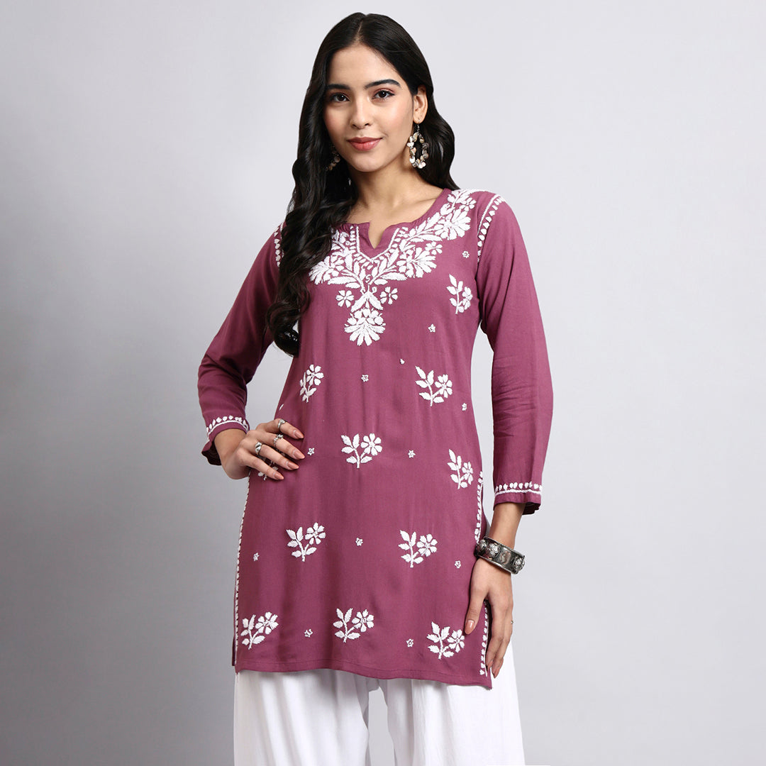 Woman wearing a purple embroidered kurta with white pants on a gray background