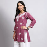Woman wearing a purple embroidered kurta with white pants on a gray background