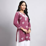 Woman wearing a purple embroidered top with white patterns on a gray background