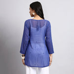 Back view of Woman wearing a blue long-sleeve top with sheer overlay on a gray background