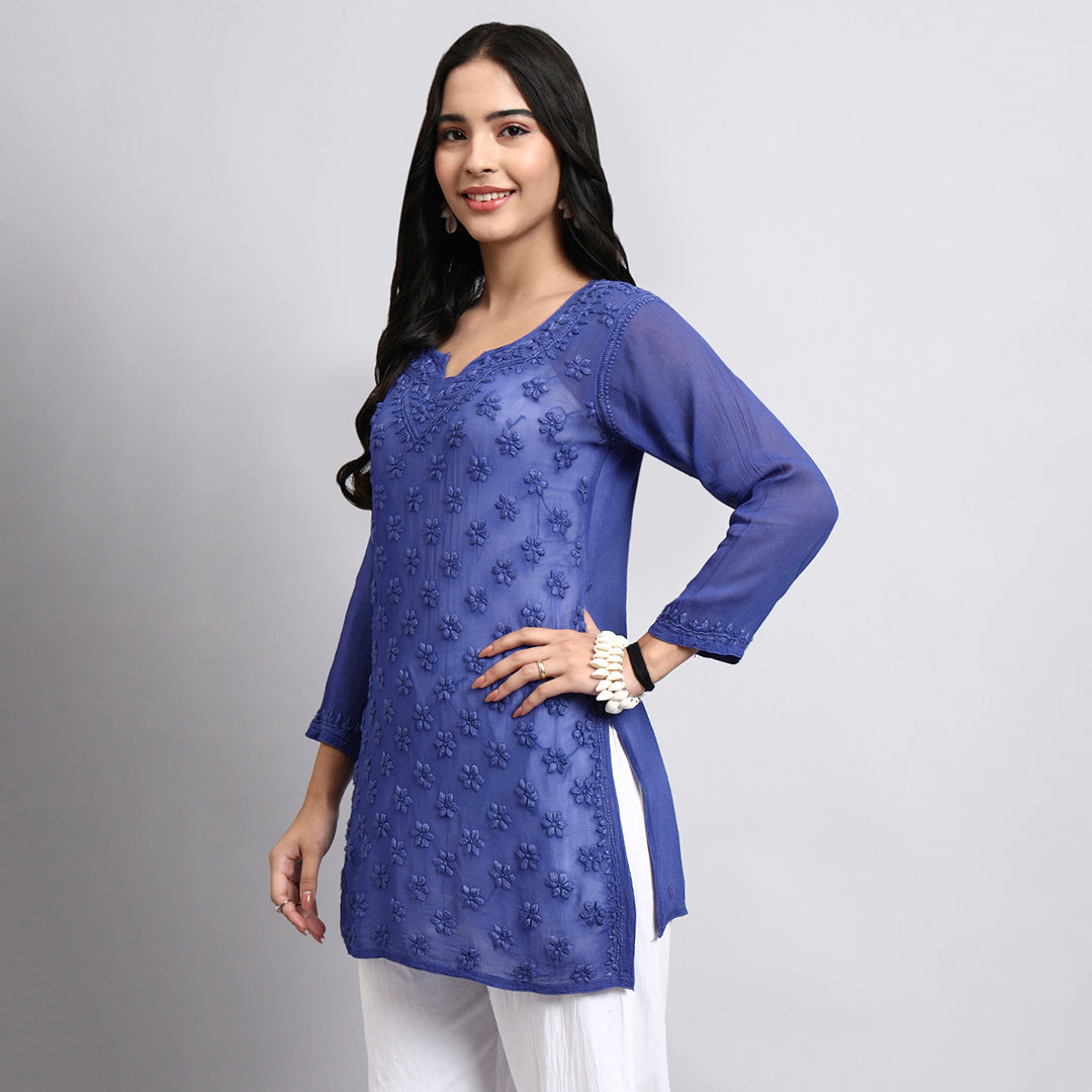 Woman wearing a blue embroidered top on a gray background