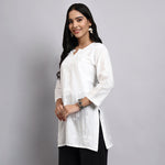 Woman wearing a white short kurta with black pants on a gray background