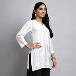 Woman wearing a white short kurta with floral patterns on a gray background