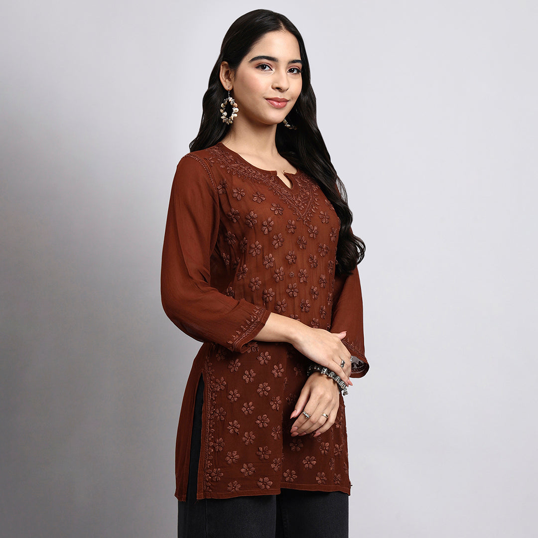 Woman wearing a brown embroidered top against a gray background