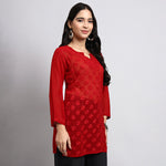 Woman wearing a red embroidered top against a gray background