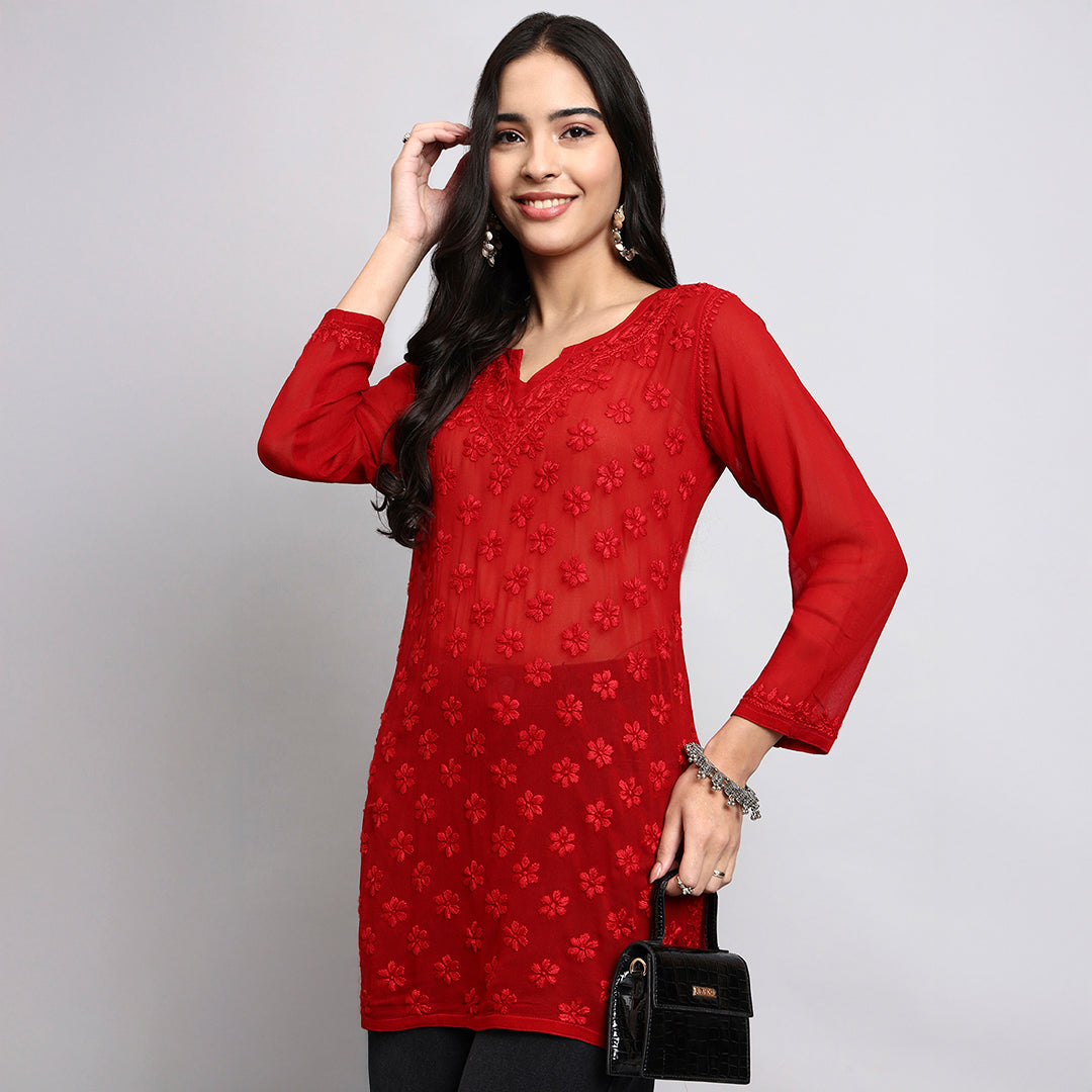 Woman wearing a red floral dress holding a black handbag against a gray background