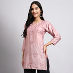 Woman wearing a pink embroidered kurta against a gray background