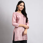 Woman wearing a pink embroidered kurta against a gray background