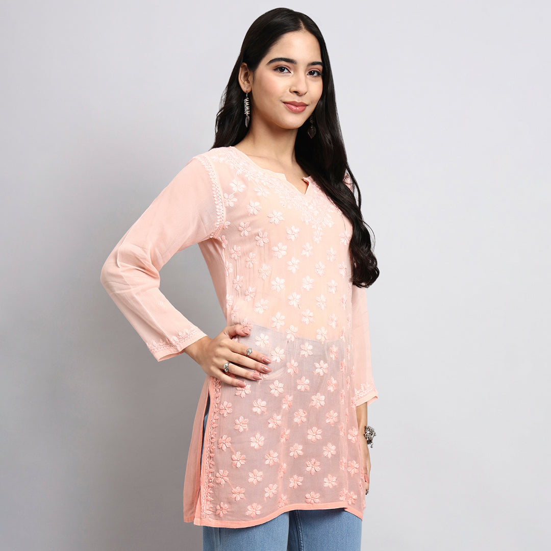 Woman wearing a light pink floral short kurta against a gray background