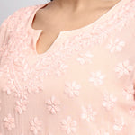 Close-up of a light pink blouse with floral embroidery on a plain background