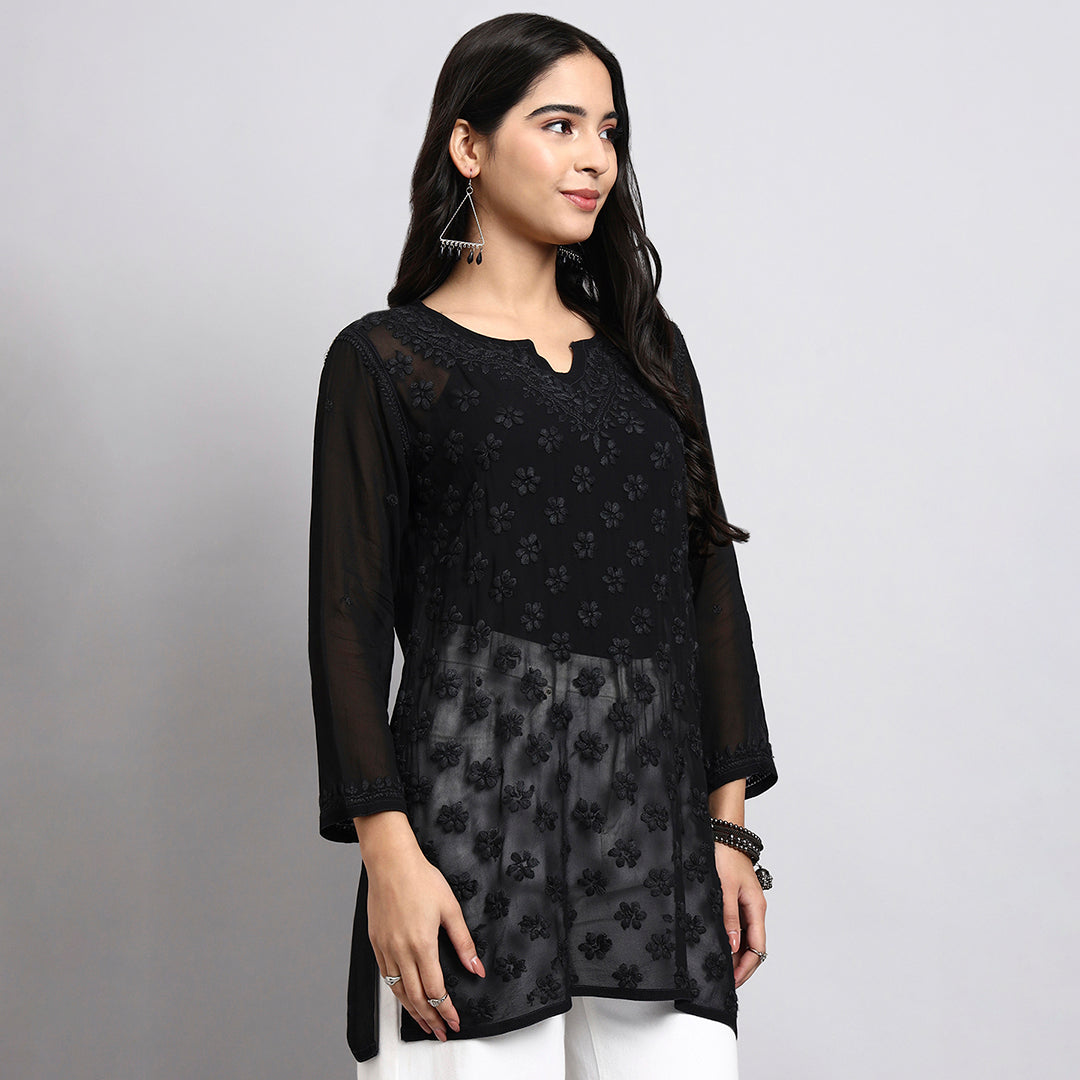 Woman wearing a black floral short kurta with sheer sleeves on a gray background.