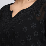Zoom view of Black embroidered garment with floral patterns on a plain background