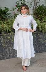 Full shot of woman in a flowy longanarkali white kurta, paired with white pants and a matching white scarf. 