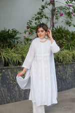 Side view of a woman in a simple yet elegant white anarkali outfit, gently touching her hair.