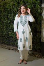 Front view of a woman in a white long mulmulkurti that has green floral embroidery on the neckline and body.