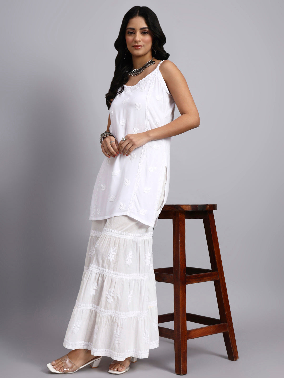 Full view of Woman wearing a white outfit standing next to a wooden stool on a gray background
