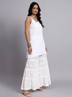 Woman wearing a white sleeveless chikankari kurti set and layered white sharara against a gray background