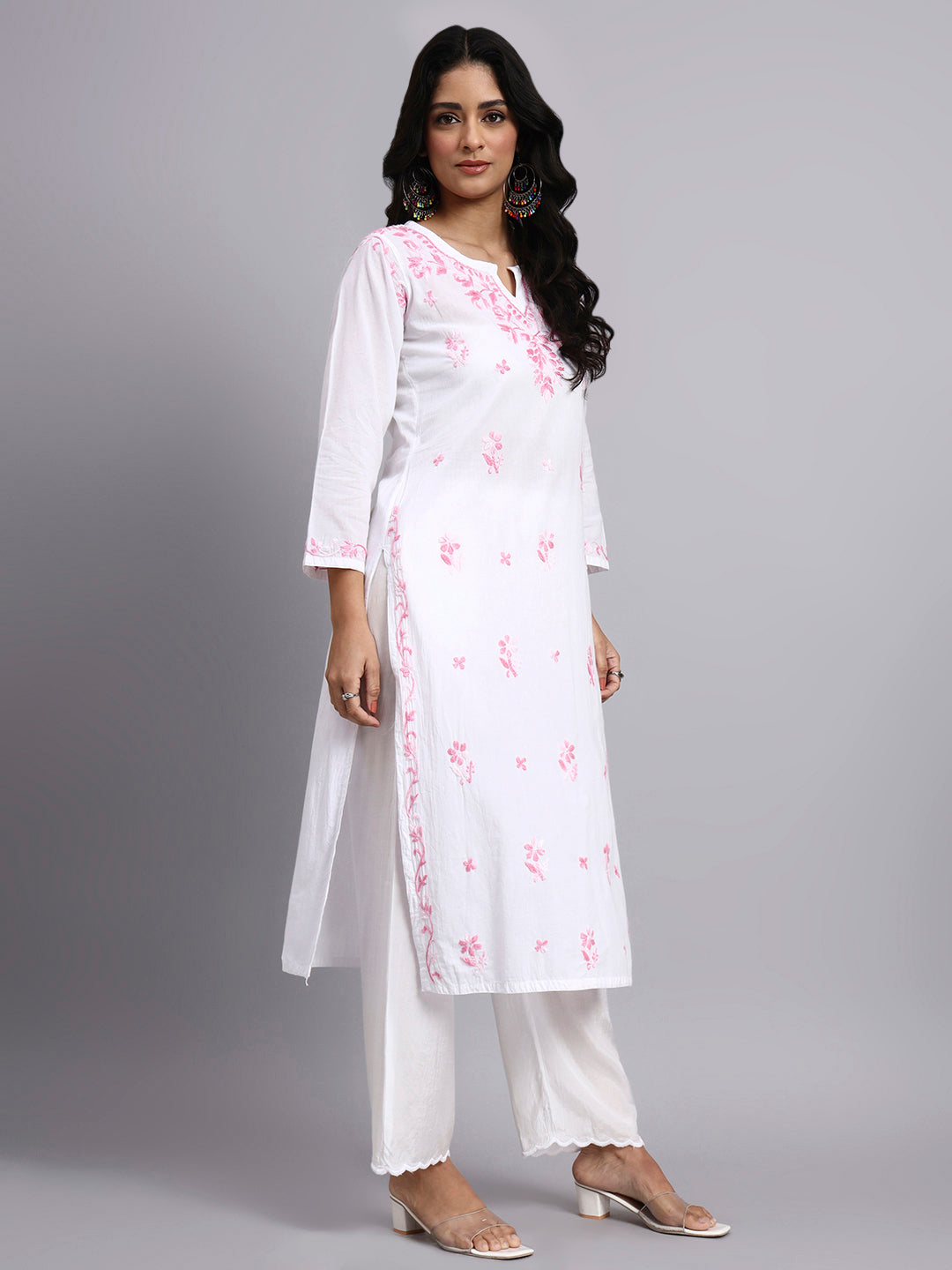 Woman wearing a white kurta with pink floral embroidery on a gray background