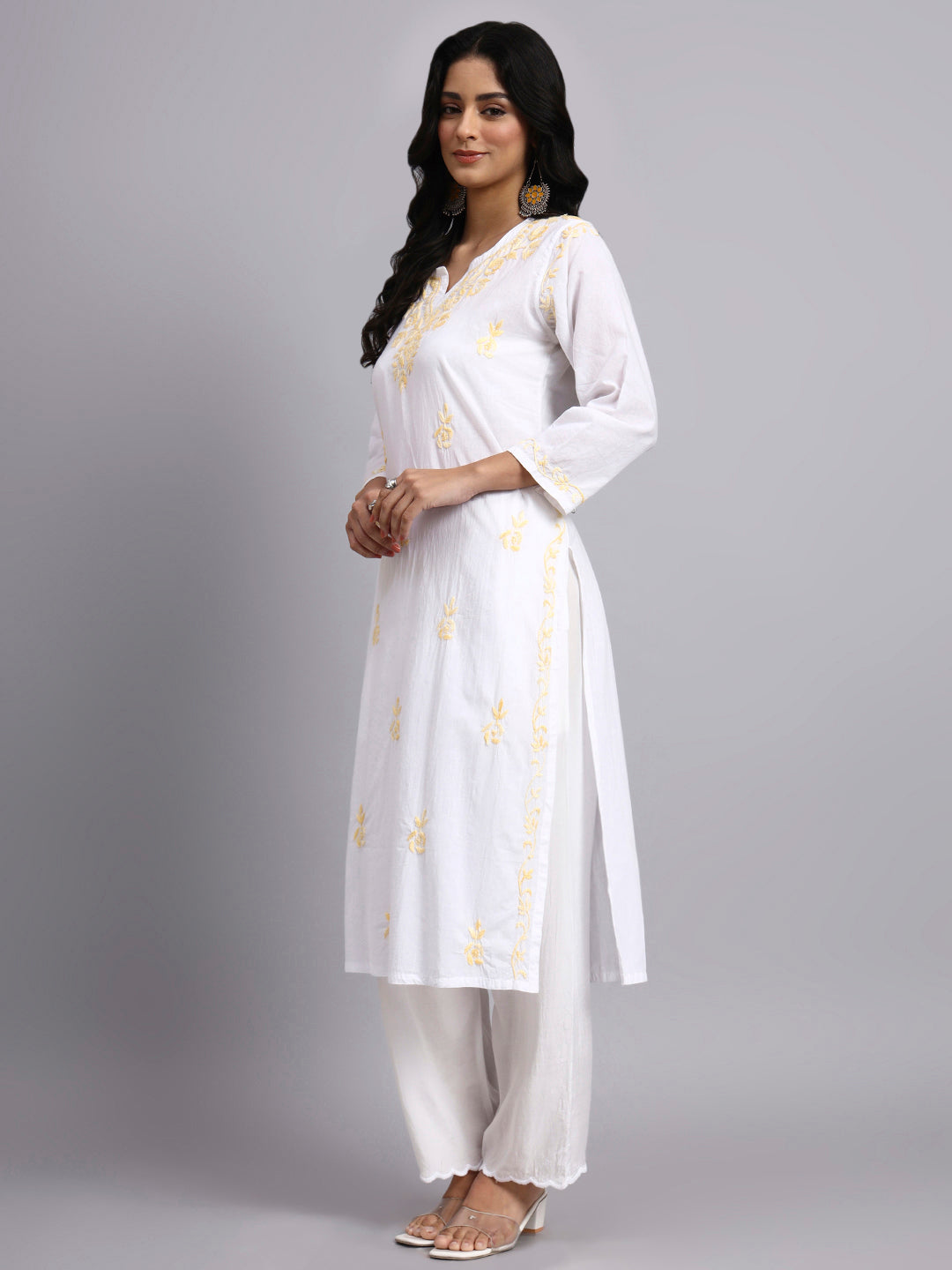 Side view of Woman wearing a white chikankari kurta with yellow patterns on a gray background