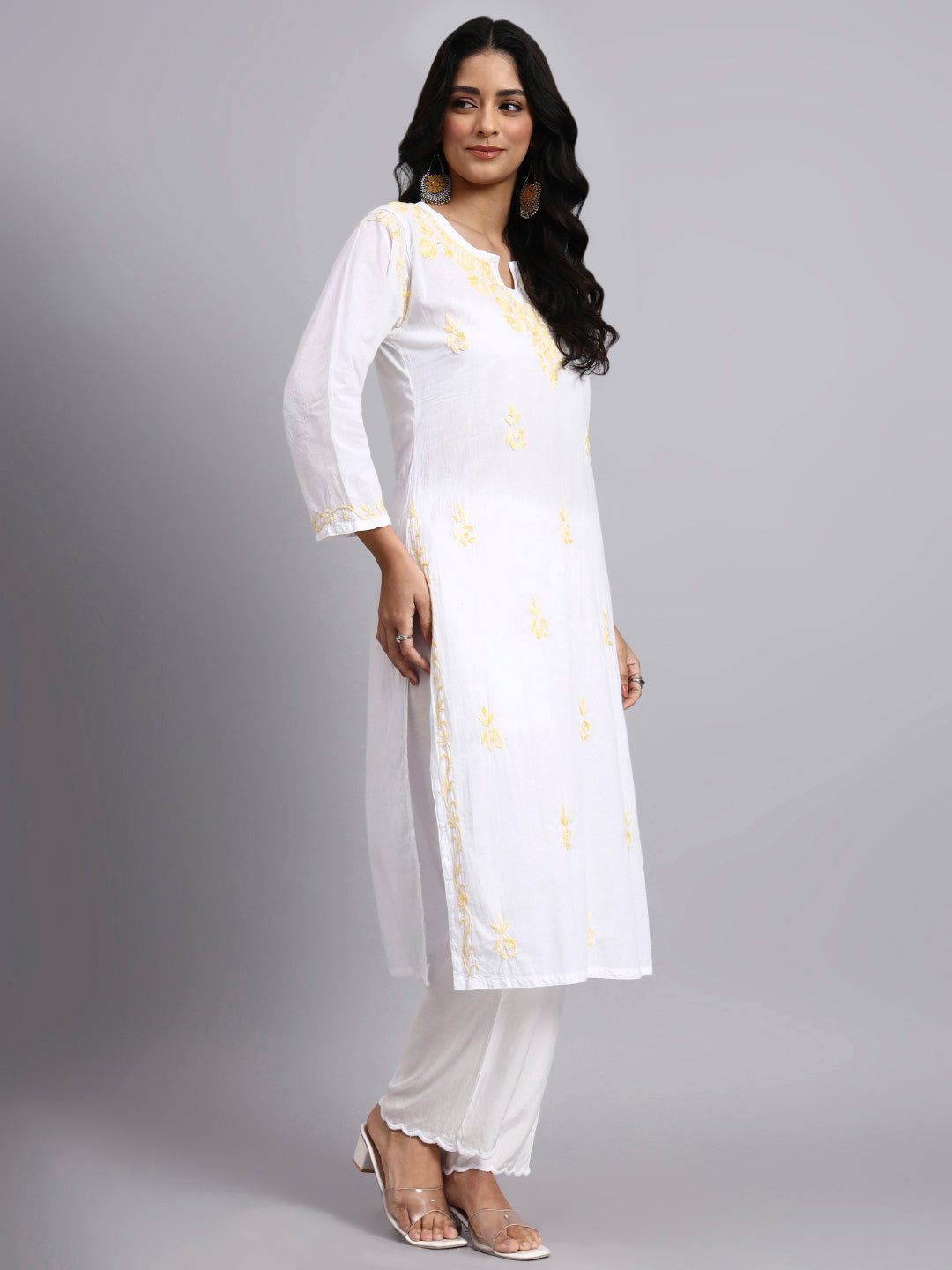 Woman wearing a white kurta with yellow patterns on a gray background