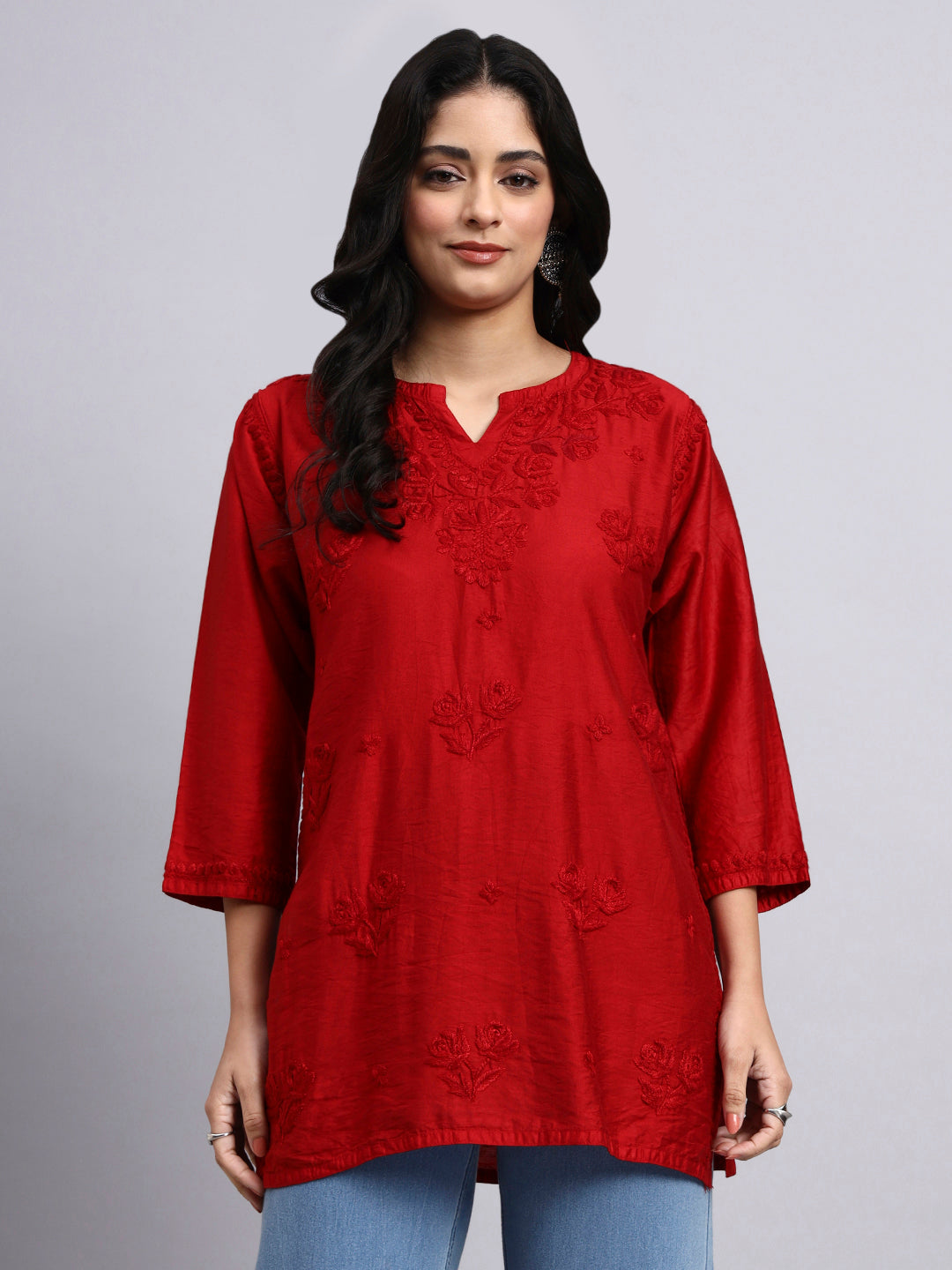 Woman wearing a red embroidered short chikankari kurti against a gray background