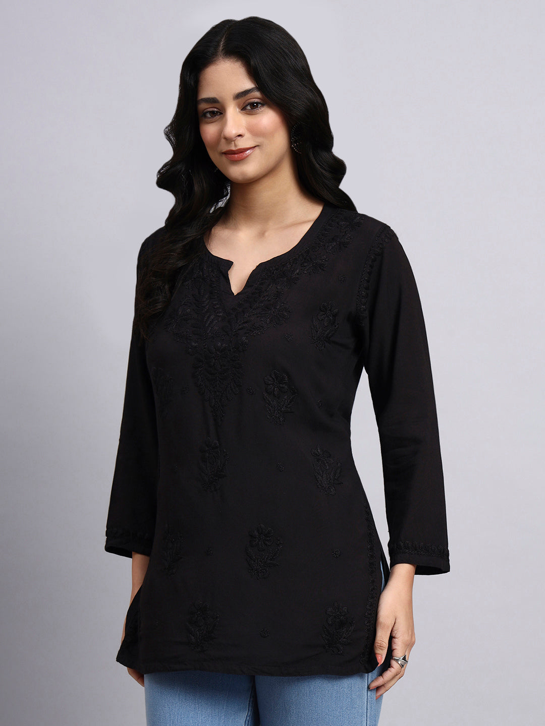 Woman wearing a black top with floral embroidery on a gray background