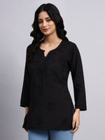Woman wearing a black top with floral embroidery on a gray background