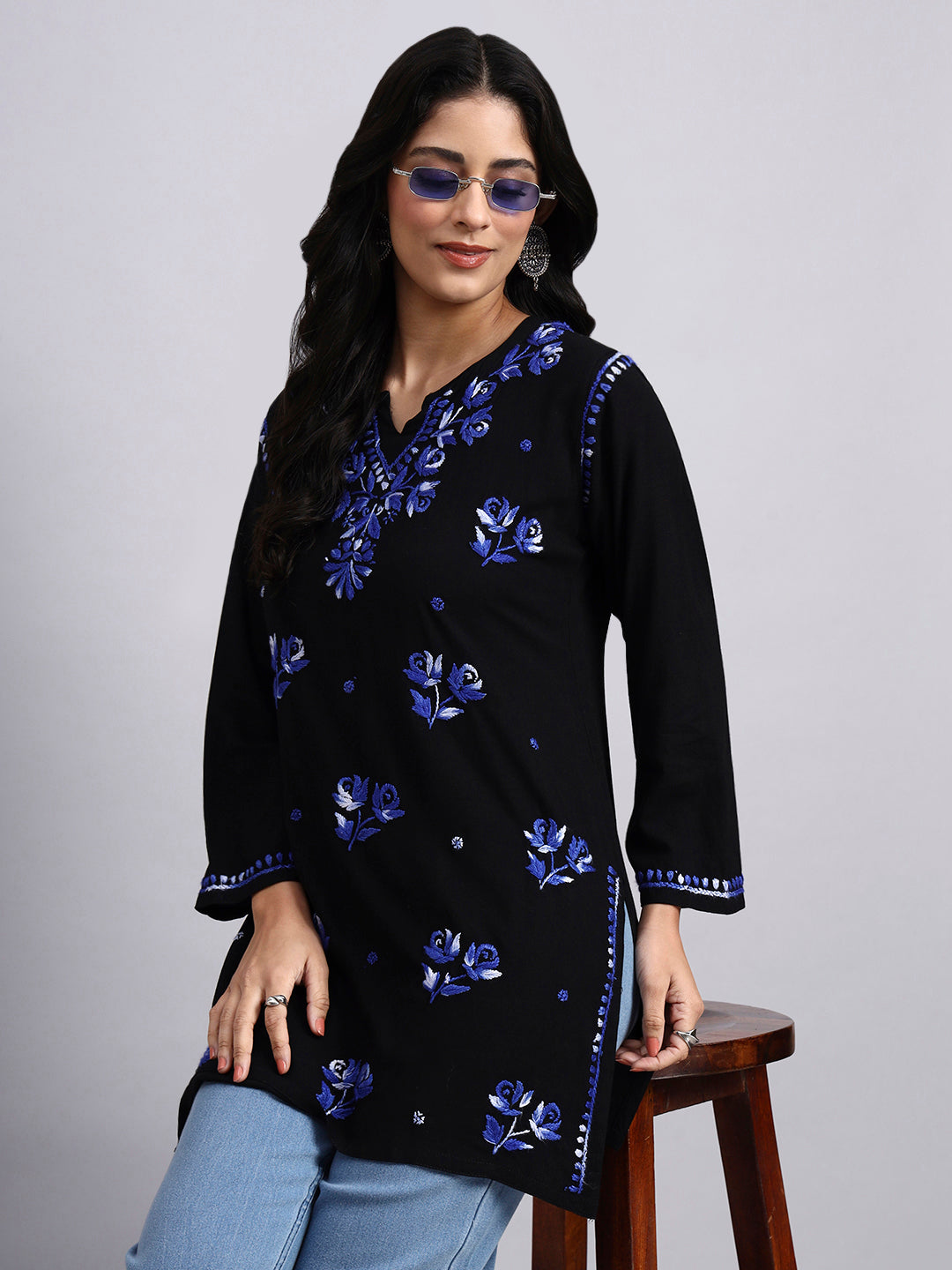 Woman wearing a black short kurta with blue floral patterns on a gray background