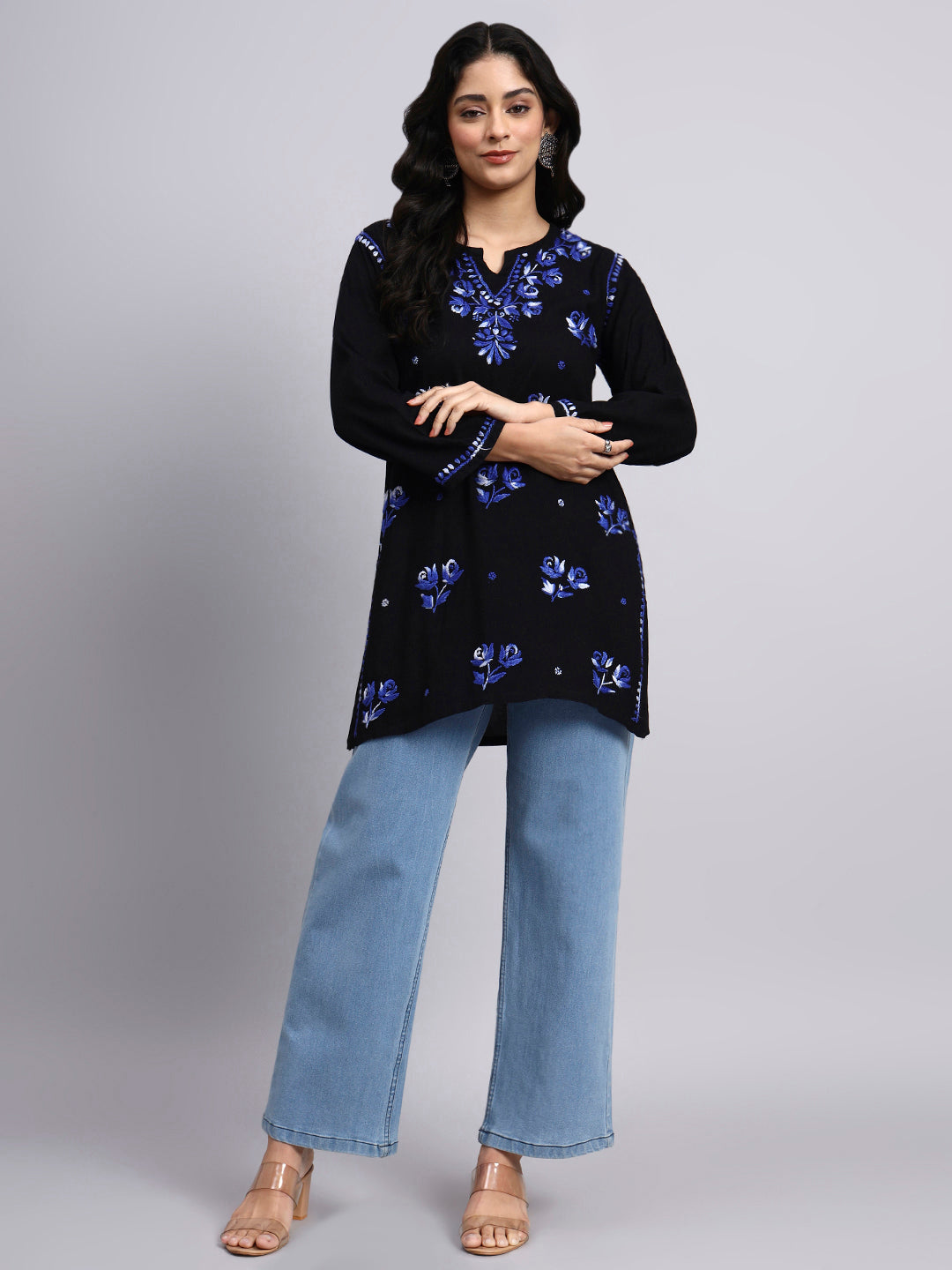 Woman wearing a black floral embroidered top and light blue jeans on a gray background