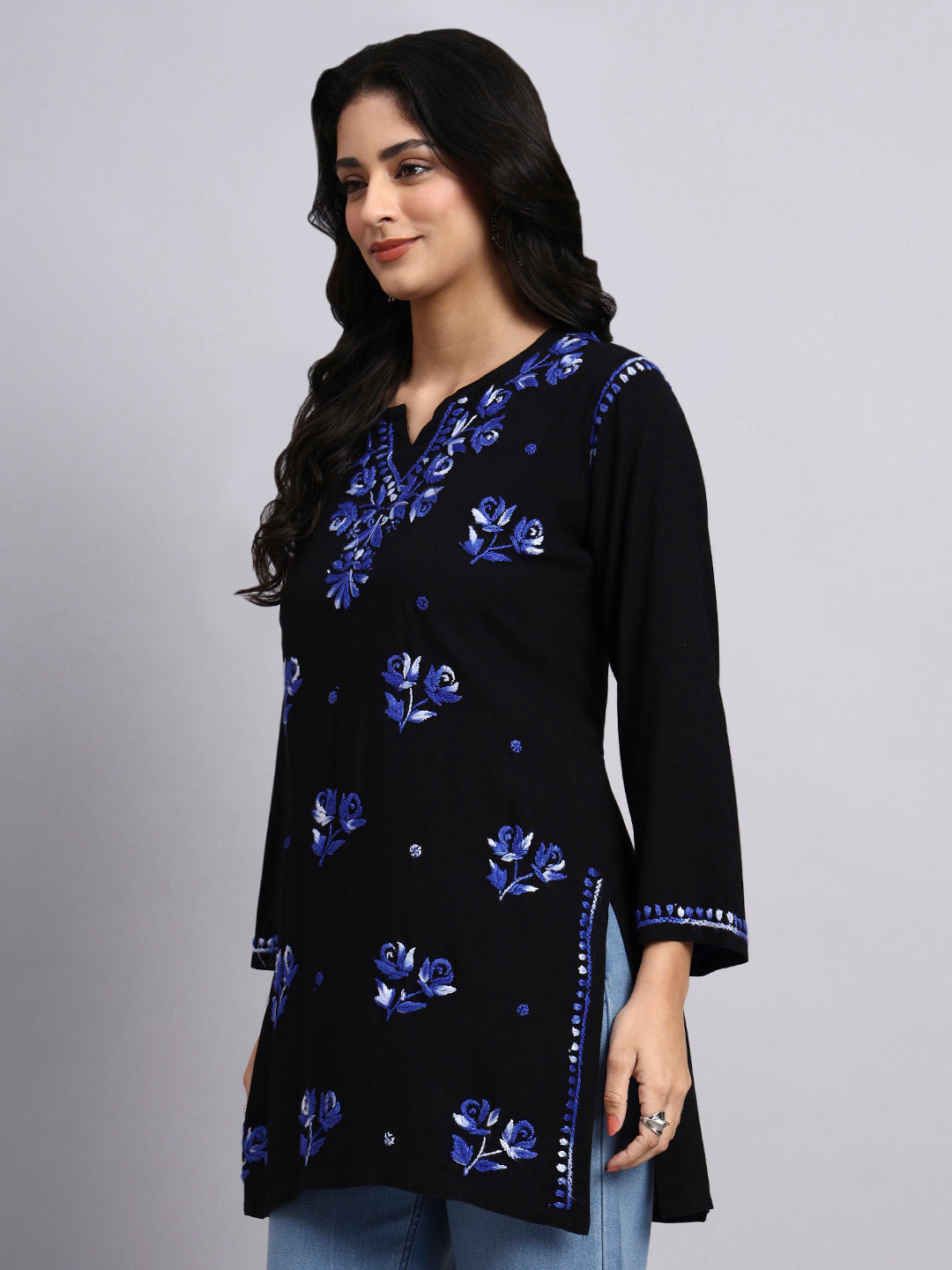 Side view of Woman wearing a black top with blue floral embroidery on a gray background