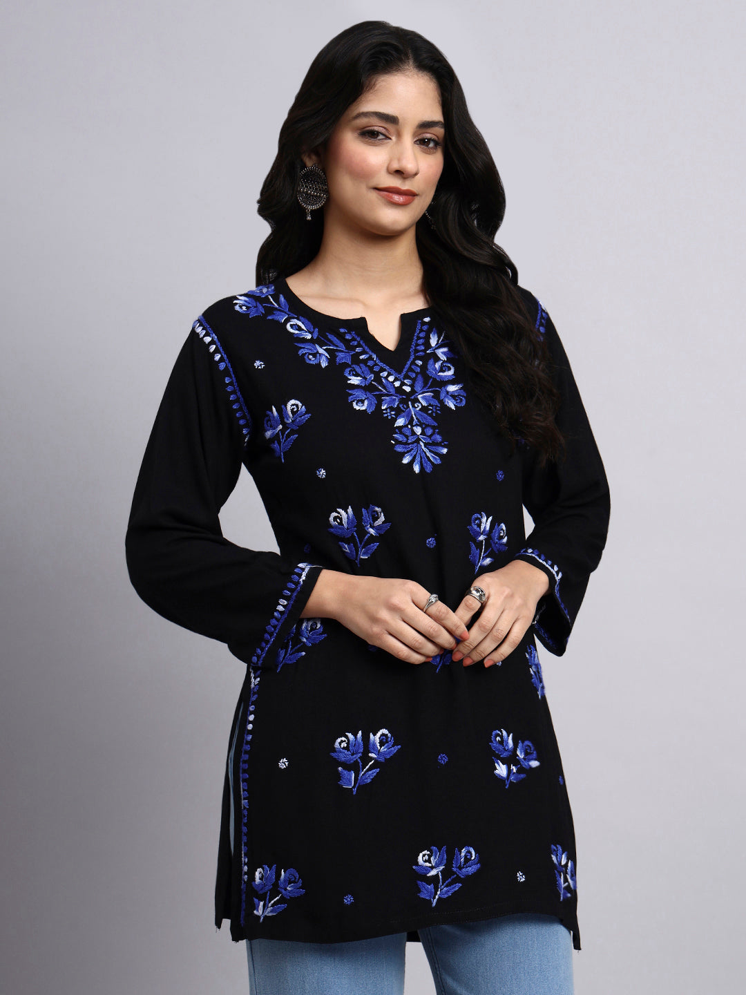 Woman wearing a black embroidered top with blue floral patterns on a gray background