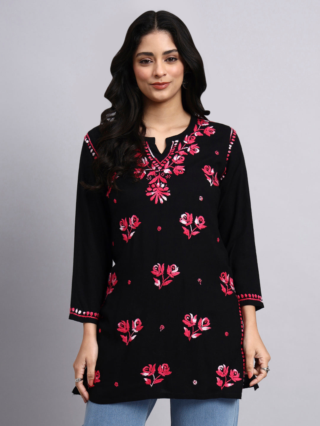 Woman wearing a black embroidered chikankari kurti with pink floral patterns on a gray background