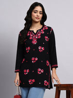 Woman wearing a black floral embroidered short kurti against a gray background