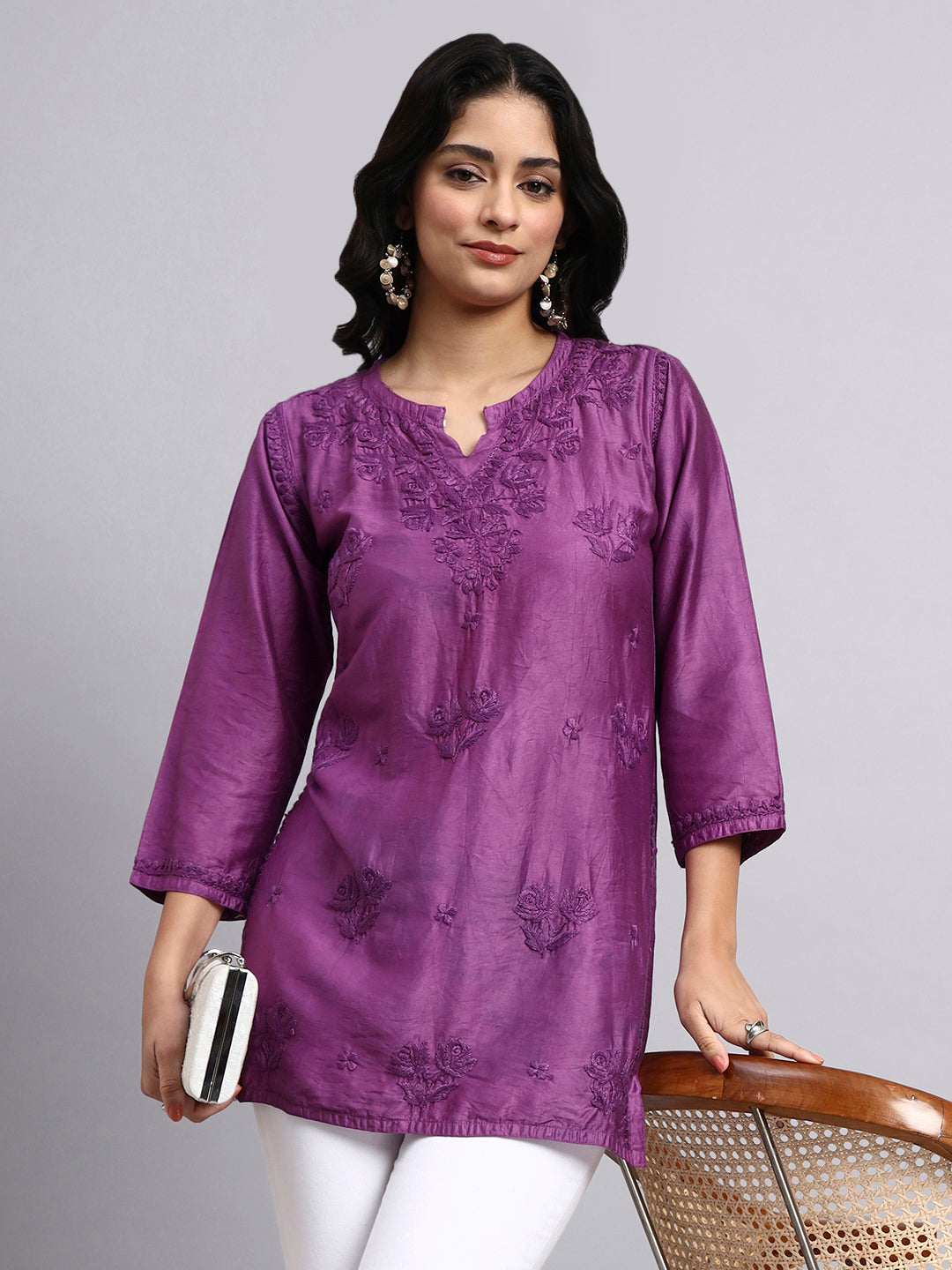 Woman wearing a purple embroidered short kurti against a gray background