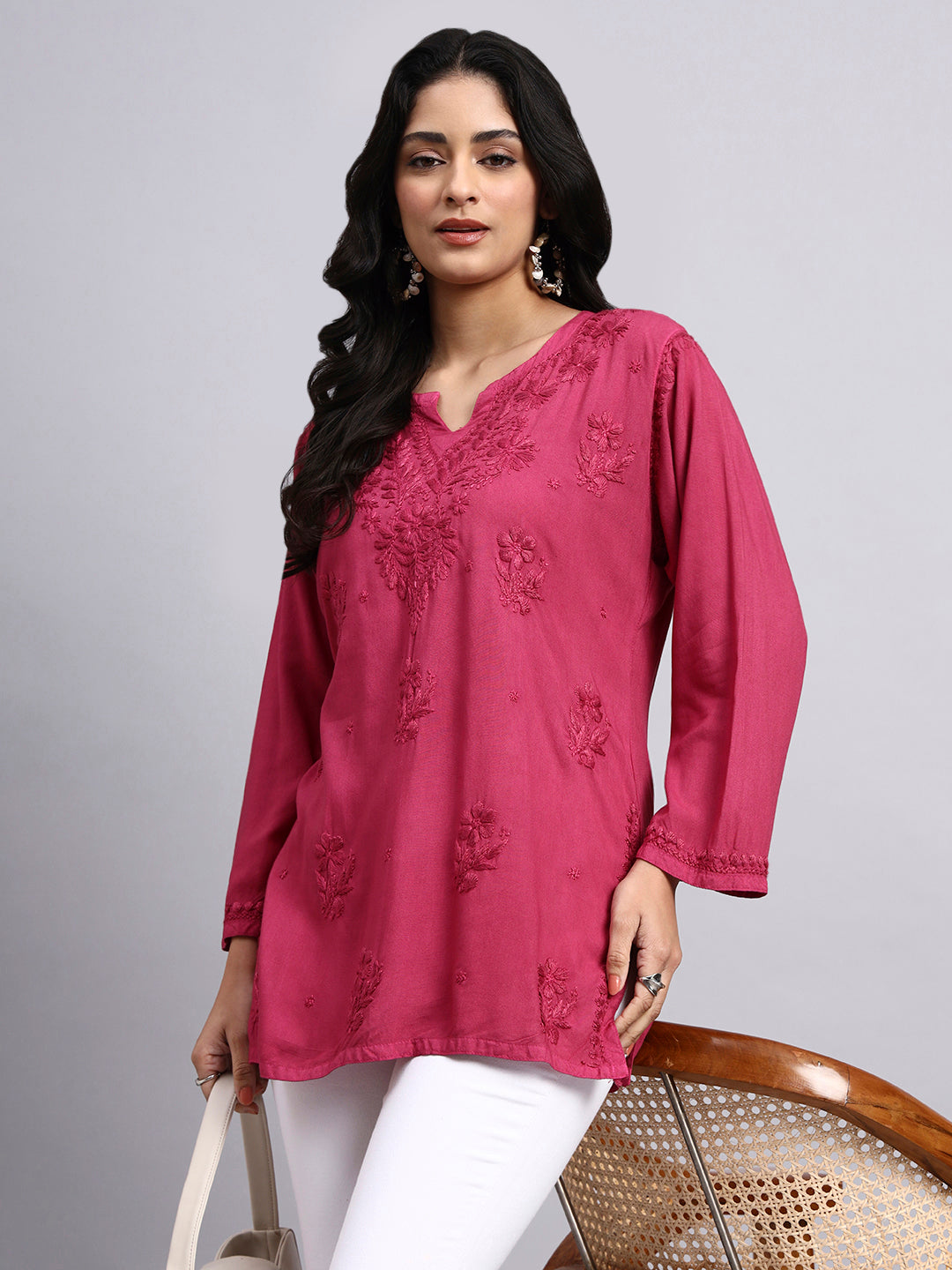 Woman wearing a pink embroidered top on a gray background
