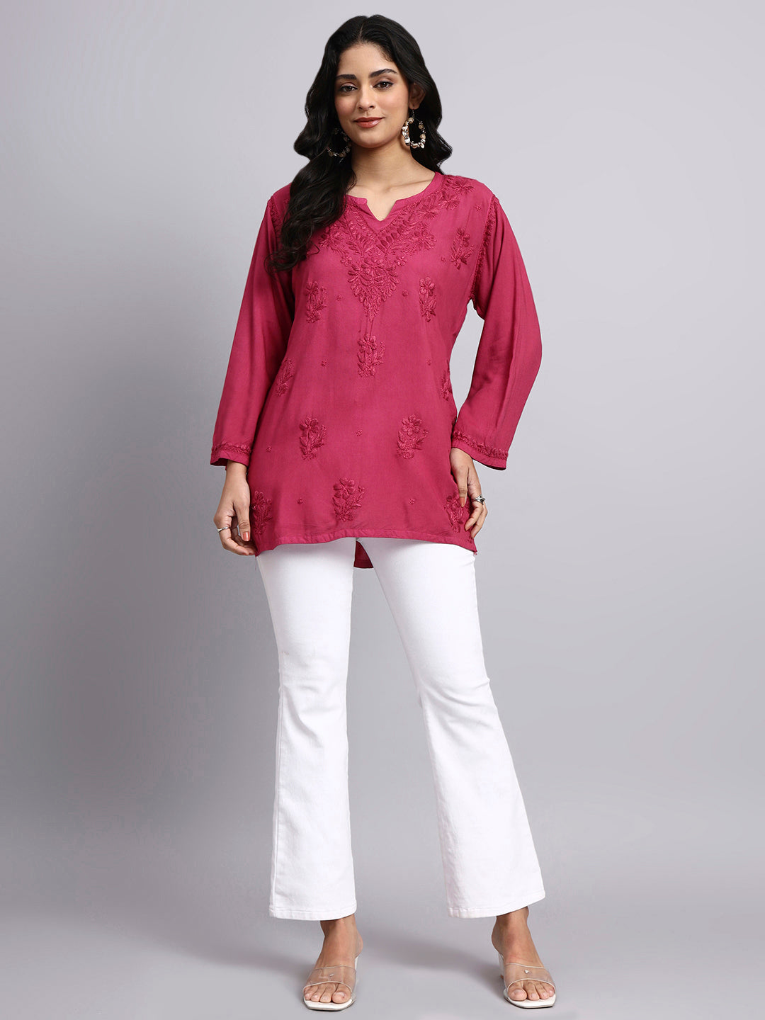 Full view of Woman wearing a pink embroidered top and white pants on a gray background