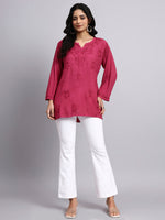 Full view of Woman wearing a pink embroidered top and white pants on a gray background