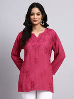 Front look of Woman wearing a pink embroidered top against a gray background