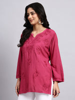Side view of Woman wearing a pink embroidered top against a gray background