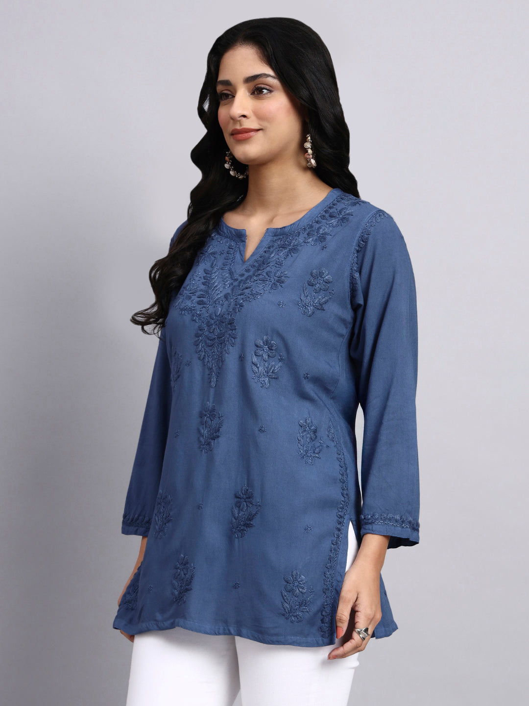 Side angle of Woman wearing a blue embroidered short kurta against a gray background