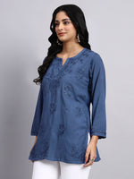Side angle of Woman wearing a blue embroidered short kurta against a gray background